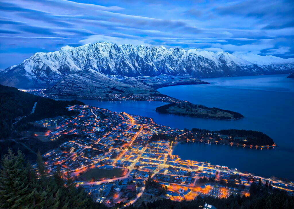 aerial view of lighted cityscape near body of water and mountains\, queenstown,